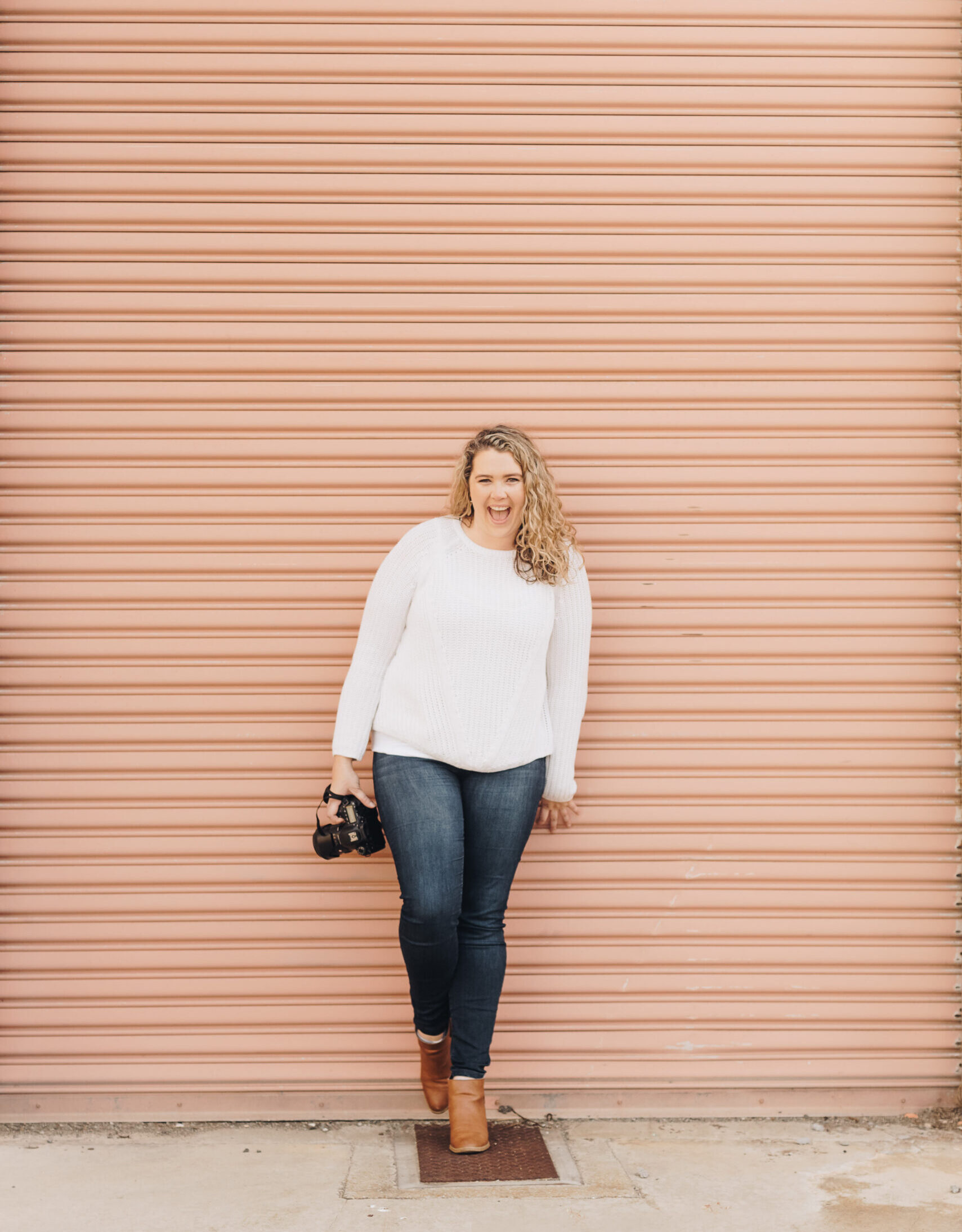 Emily, Founder of Woodall Creative Co stands against a pink background holding her camera.