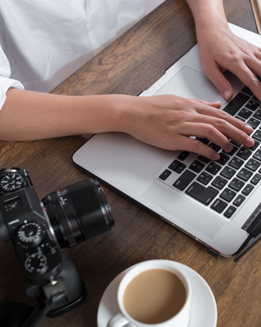woman types on laptop with camera and coffee sitting nearby